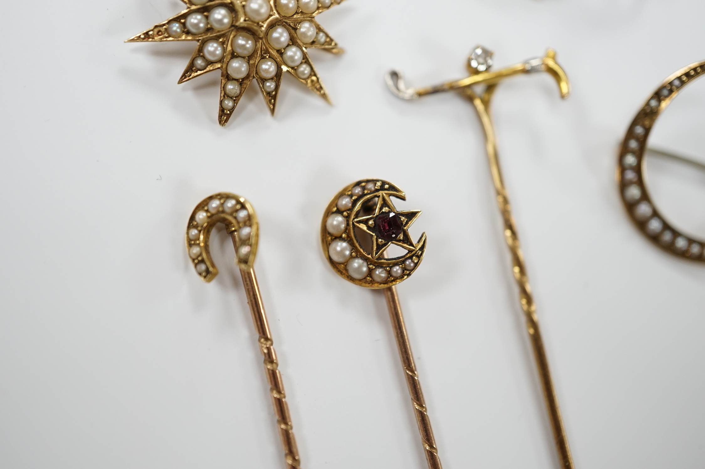 Three early to mid 20th century yellow metal and seed pearl set brooches, largest 34mm, two similar stick pins and a diamond set riding crop stick pin.